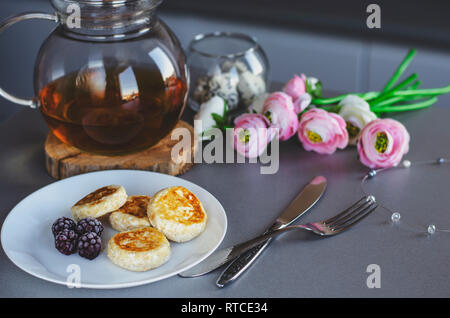 Una sana colazione a base di frittelle di ricotta con frutti di bosco e tè verde in un bicchiere tè pentola. Copia dello spazio. La dieta dolce concetto. Foto Stock