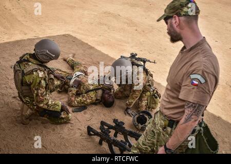 Un ceco delle forze speciali soldato osserva i soldati del Mali come essi tendono a simulare un soldato ferito durante Flintlock 2019 formazione medica in Loumbila, Burkina Faso Feb 16, 2019. La formazione medica fornisce i soldati del Mali la possibilità di ottenere le mani su esperienza medica dalla multinazionale di forze speciali militari. Foto Stock