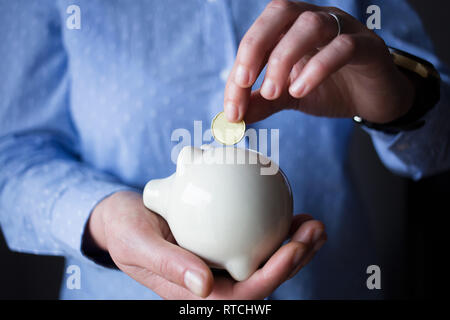 Persona è l'inserimento di una moneta d'oro in una ceramica nera salvadanaio Foto Stock