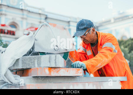 Mosca, Russia - Agosto 14, 2015: un builder taglia un pezzo di pietra di granito su una macchina a sega circolare. La ricostruzione del pavimento di piastrelle nel capitale Foto Stock