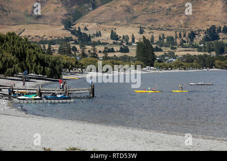 Persone in giallo kayak sul lago Wanaka dal jetty di turisti e di jet sci su una soleggiata giornata estiva, Wanaka, Nuova Zelanda Isola del Sud Foto Stock