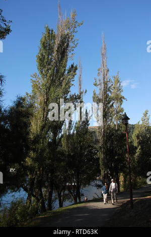 Coppia giovane a piedi lungo un sentiero in Giardini di Queenstown in serata sole dal lago Wakatipu, Queenstown, New Zealand Nuova Zelanda Isola del Sud Foto Stock