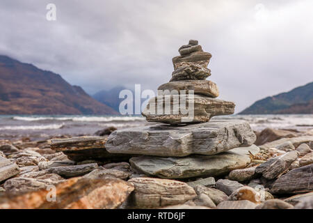 Un piccolo tumulo di pietre sulla riva del lago Wakatipu, Queenstown. Nuova Zelanda Isola del Sud con picco di Cecil e Walter picco in background Foto Stock