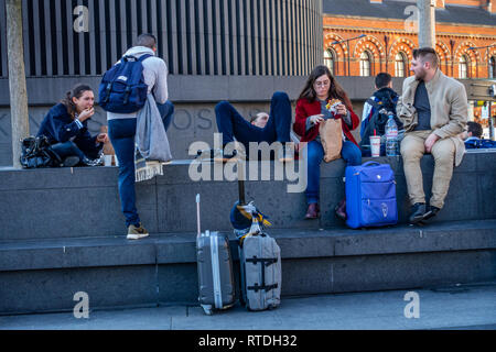 Gruppo di amici seduti a mangiare fuori la stazione di Kings Cross a Londra, Inghilterra Foto Stock