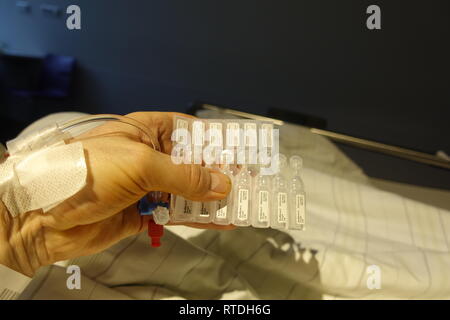 Uomo che indossa un abito ospedale con un IV di linea e di catetere inserito di sua mano. Foto Stock