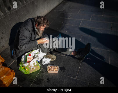 Senzatetto uomo appoggiato su di una parete e di seduta al di fuori di Kings Cross stazione ferroviaria di Londra, Inghilterra Foto Stock