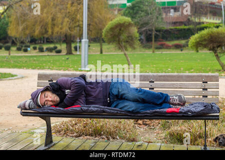 Senzatetto uomo dorme sul banco a park Foto Stock