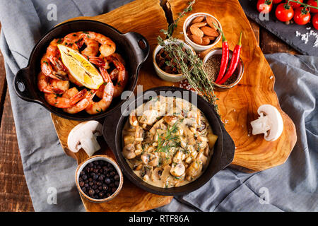 Gran fritto di gamberi in salsa di pomodoro con olio di oliva,funghi in salsa di panna julienne, champignon, prodotti per la cottura sul tavolo di legno sfondo Foto Stock