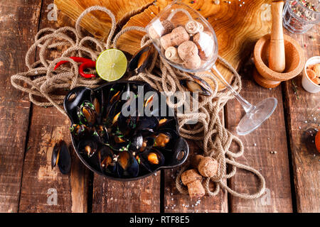 Bollito di cozze in piatto di rame per la cottura su sfondo di legno, vicino a fune e di prodotti per la cottura di close-up Foto Stock