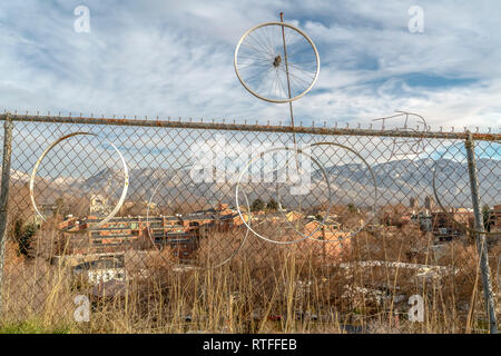 Bike cerchioni ruota appesi a rusty catena collegamento recinto. Cerchi di ruote di bicicletta appesa su un arrugginito catena collegamento recinto con case e montagna in background. C Foto Stock