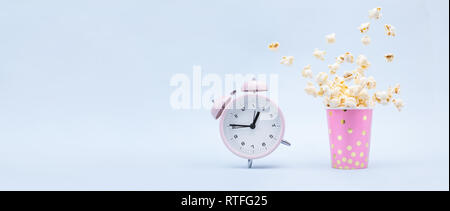 Flying Popcorn in un luminoso vetro e una Suoneria sveglia su uno sfondo blu. Tempo per un concetto di divertimento. Banner Foto Stock