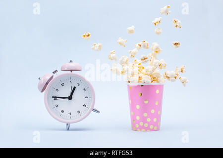 Flying Popcorn in un luminoso vetro e una Suoneria sveglia su uno sfondo blu. Tempo per un concetto di divertimento. Foto Stock