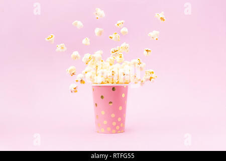 Flying Popcorn in un luminoso vetro e su un sfondo rosa. Spazio di copia Foto Stock