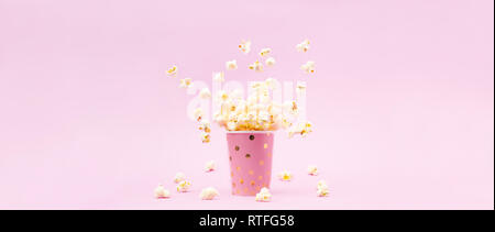 Flying Popcorn in un luminoso vetro e su un sfondo rosa. Spazio di copia Foto Stock