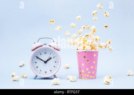Flying Popcorn in un vetro luminoso e sveglia su uno sfondo blu. Tempo per un concetto di divertimento. Foto Stock