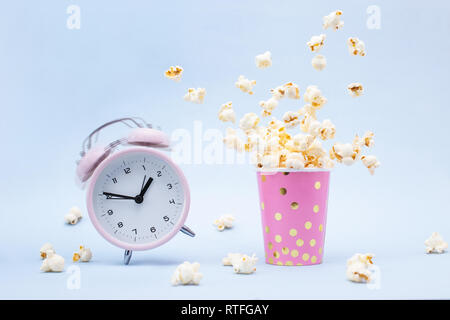 Flying Popcorn in un luminoso vetro e una Suoneria sveglia su uno sfondo blu. Tempo per un concetto di divertimento. Foto Stock