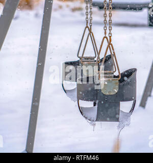 Coperta di neve parco giochi con altalene per bambini in Utah. Close up di altalene per bambini contro la coperta di neve la massa d'inverno. Svuotare il parco giochi in Alba, U Foto Stock