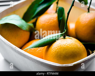 Alcune arance con foglie in un cestello, Arancione Tangerini in un cesto su uno sfondo bianco. Foto Stock