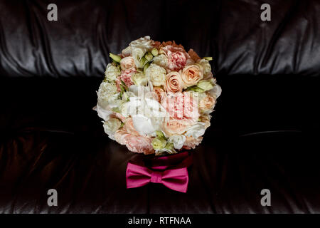 Nozze cravatta a farfalla e bouquet di bridewith rosa e rose bianche sdraiato sul lettino su uno sfondo scuro. Foto Stock