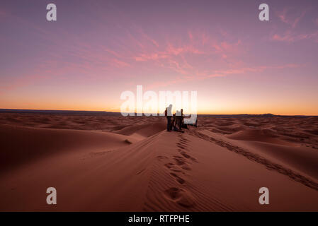 La gente sta guardando la sorprendente alba sulle dune Erg Chebbi nel deserto del Sahara . Bella sabbia paesaggio con incredibile cielo. Merzouga, Marocco Foto Stock