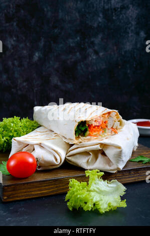 Delizioso sandwich shawarma su uno sfondo nero. Burrito si avvolge con grigliate di carne di pollo e verdure, verdi. Fajitas, pane pita. Medio tradizionale Foto Stock