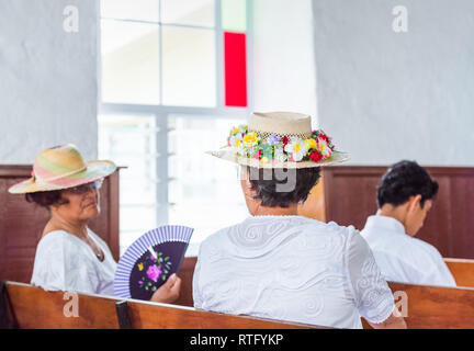 ARUTANGA, Aitutaki, COOK ISLAND - 30 settembre 2018: la donna in un cappello in una chiesa cattolica nel servizio. Con il fuoco selettivo. Vista posteriore Foto Stock