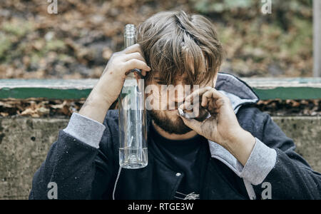 Close up man mano un bicchiere di vodka. Bevuto giovani. (Alcolismo, dolore, peccato, disperazione, problema sociale della dipendenza concetto) Foto Stock