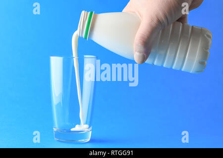 Versare il latte dalla bottiglia di plastica in vetro su sfondo blu Foto Stock