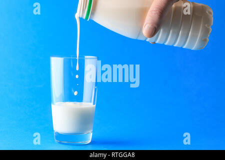 Versare il latte dalla bottiglia di plastica in vetro su sfondo blu Foto Stock