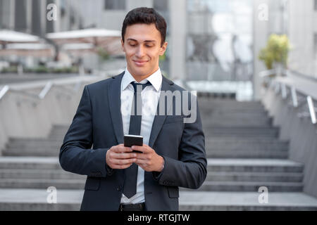 Young business man standing sulla strada di città il controllo sociale dei media sullo smartphone durante il tempo libero a sorridere gioiosa Foto Stock