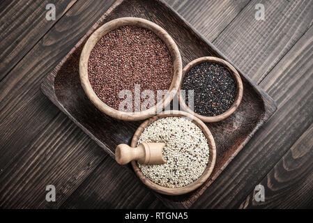 Diversi tipi di grezzo di quinoa semi nella ciotola di legno su sfondo di legno vista superiore Foto Stock