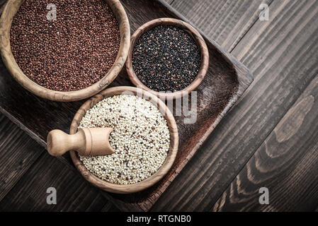 Diversi tipi di grezzo di quinoa semi nella ciotola di legno su sfondo di legno vista superiore Foto Stock