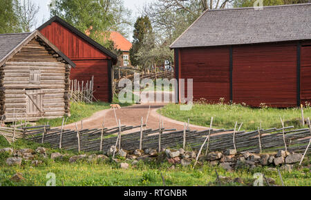 Due gatti a una strada di campagna con una vecchia casa colonica e roundpole tradizionale recinto nel villaggio rurale di Stensjo in Smaland, Svezia e Scandinavia Foto Stock