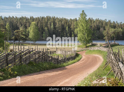 Il pittoresco paese strada che conduce a un lago in un bellissimo paesaggio rurale tradizionale con roundpole svedese recinzioni, Smaland, Svezia e Scandinavia. Foto Stock