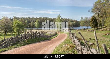 Il pittoresco paese strada che conduce a un lago in un bellissimo paesaggio rurale tradizionale con roundpole svedese recinzioni, Smaland, Svezia e Scandinavia. Foto Stock