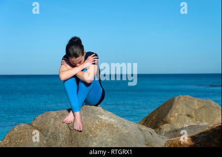 Premuto donna seduta sulle rocce in riva al mare Foto Stock