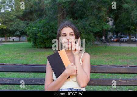 Bella femmina studente è in possesso di un libro e di pensare a qualcosa. La donna ha un'idea interessante. Foto Stock