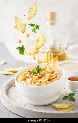 Hummus ciotola e caduta di ingredienti - i ceci, il prezzemolo, la paprika e il chip. Alimentare il concetto di levitazione. Flying ingredienti. Foto Stock