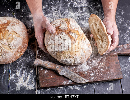 Lo chef in un nero uniforme tenendo freschi cotti al forno caldo pane tondo al di sopra della tavola nelle sue mani Foto Stock