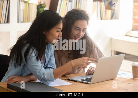 Diversi giovani studenti lavoratori parlando in ufficio guardando il computer portatile Foto Stock