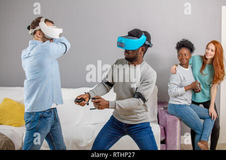 Gruppo di multirazziale maschio femmina amd gli studenti la riproduzione di gioco virtuale utilizzando occhiali VR, divertirsi insieme ay home - Virtual omg la realtà e portatile di Foto Stock