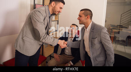 Tre uomini di affari sorridente e stringono le mani mentre è seduto in un comodo ambiente di ufficio Foto Stock