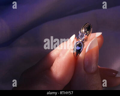 Chiusura del diamante elegante anello al dito con sciarpa grigio Sfondo. Corona diamantata. Foto Stock