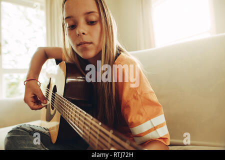 In prossimità di una ragazza adolescente a suonare la chitarra seduti a casa. Ragazza giovane facendo il suo lezioni di chitarra a casa. Foto Stock