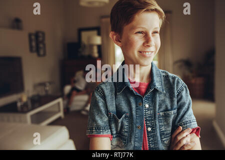 Ritratto di un sorridente ragazzo accanto a casa con le braccia incrociate. Ragazzo accanto a casa e guardando lontano mentre i suoi amici seduti insieme in backgrou Foto Stock