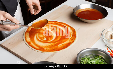 Aggiunta di salsa. Lo chef prepara la pizza italiana nel ristorante Foto Stock