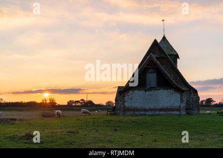 Tramonto Tramonto sopra la chiesa solitaria nella palude, il Thomas A Beckett in legno e chiesa di mattoni a Fairfield, Romney Marsh. Pecore al pascolo. Foto Stock