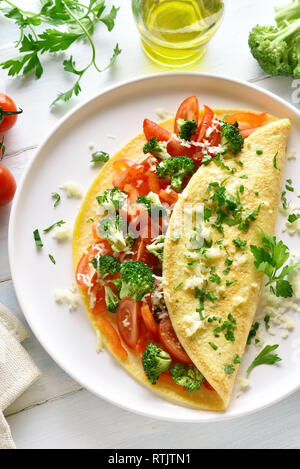 Riempite la frittata con pomodori, peperone rosso e i broccoli sulla luce sullo sfondo di legno. Alimentazione sana alimenti per la colazione. Omelette ripiene di verdure Foto Stock