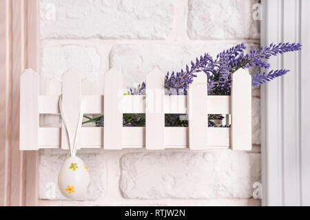 Uovo di Pasqua appeso su un ripiano decorativo - un recinto su un bianco muro di mattoni Foto Stock