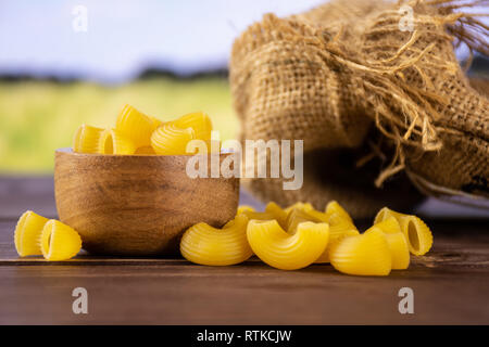 Sacco di tutta la pasta grezza pipe rigate varietà con ciotola di legno verde con campo di grano Foto Stock